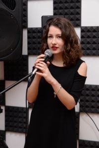 Девушка в черном платье проходит обучение в вокальной студии